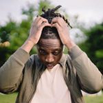 Startup Mistakes - Upset young African American male freelancer clutching head with hands after failure in project while working remotely in park